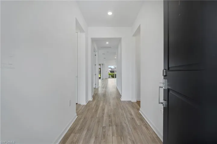 Entryway featuring a dark paneled door with contemporary hardware, wood-finish flooring, recessed lighting, and crisp white walls