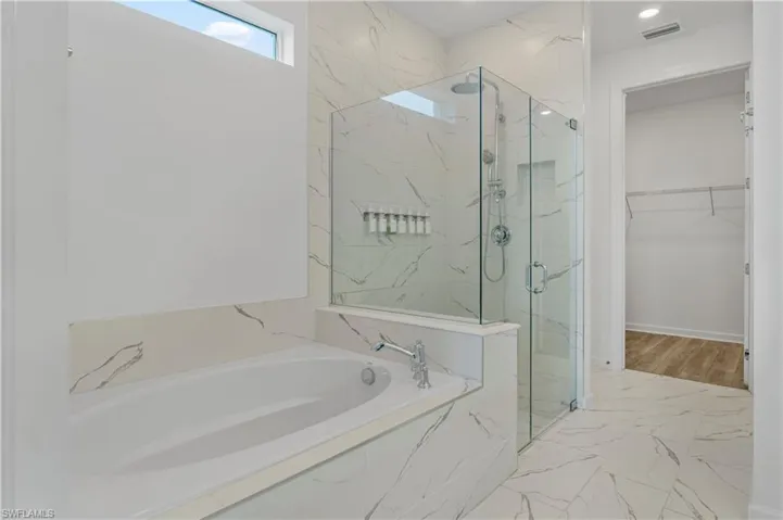 Soaking tub with deck-mounted chrome fixtures, glass-enclosed shower with a rainfall showerhead, and a tiled shower niche