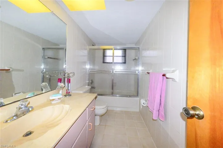 Full bathroom with tile walls, vanity, enclosed tub / shower combo, and toilet