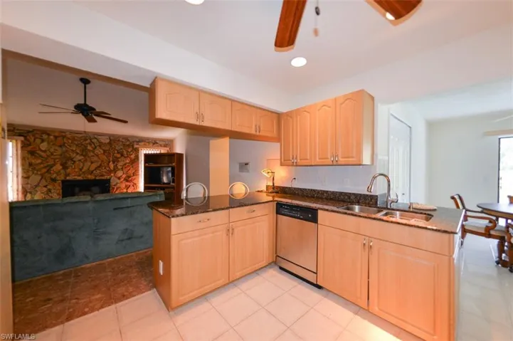 Kitchen with stainless steel dishwasher, sink, kitchen peninsula, and dark stone countertops