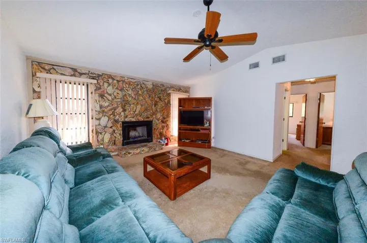 Living room with lofted ceiling, a fireplace, light colored carpet, and ceiling fan