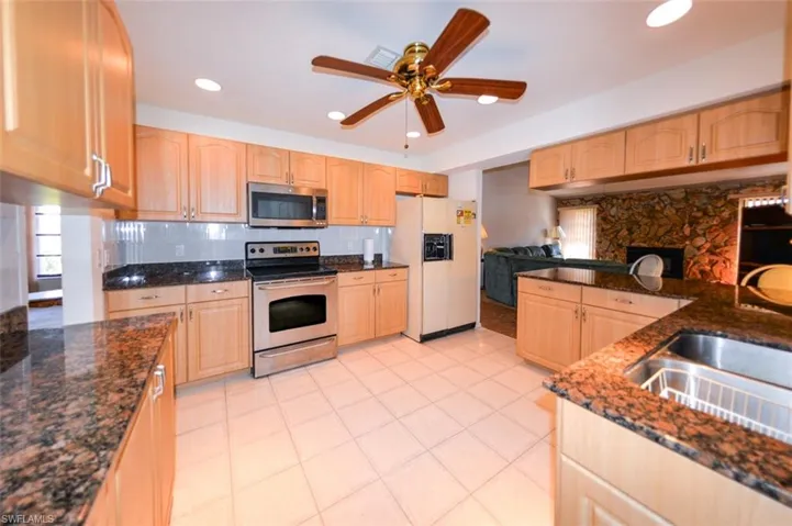 Kitchen with light brown cabinets, stainless steel appliances, dark stone countertops, sink, and ceiling fan