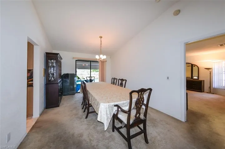 Carpeted dining space with a notable chandelier and vaulted ceiling