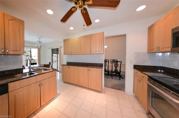 Kitchen featuring sink, backsplash, ceiling fan, stainless steel appliances, and dark stone countertops