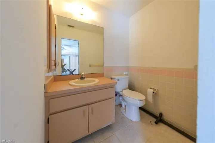 Bathroom featuring toilet, vanity, tile patterned floors, and tile walls