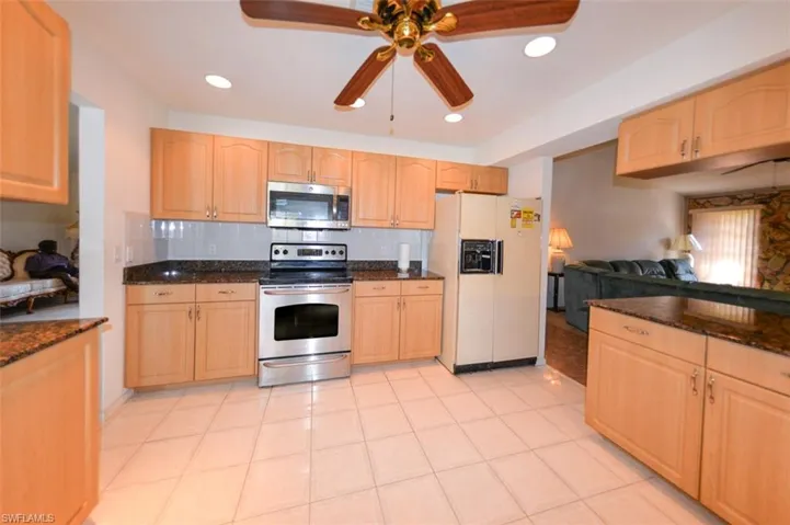Kitchen with light brown cabinets, decorative backsplash, ceiling fan, appliances with stainless steel finishes, and dark stone counters