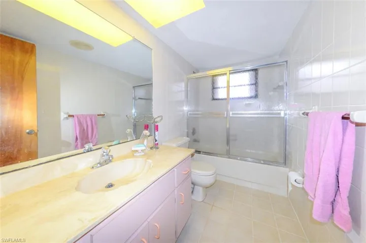 Full bathroom featuring bath / shower combo with glass door, tile walls, toilet, vanity, and tile patterned flooring