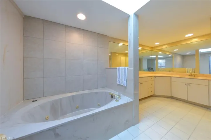 Bathroom with tile walls, vanity, tiled bath, and tile patterned floors