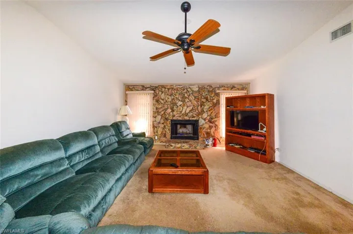 Carpeted living room with vaulted ceiling, a fireplace, and ceiling fan