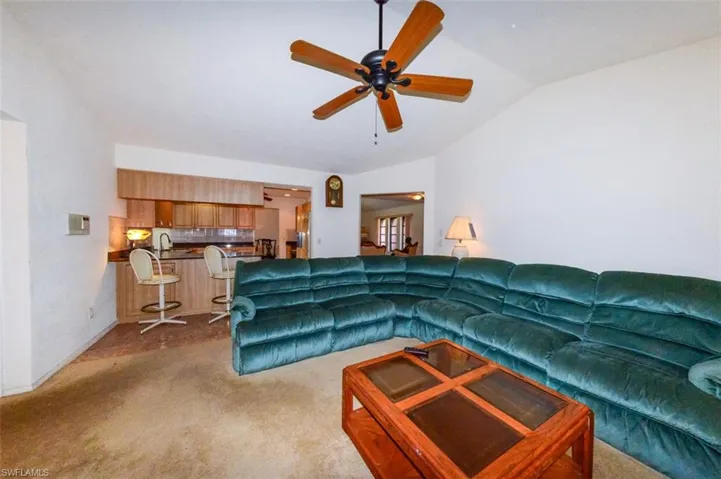 Carpeted living room featuring sink, ceiling fan, and vaulted ceiling