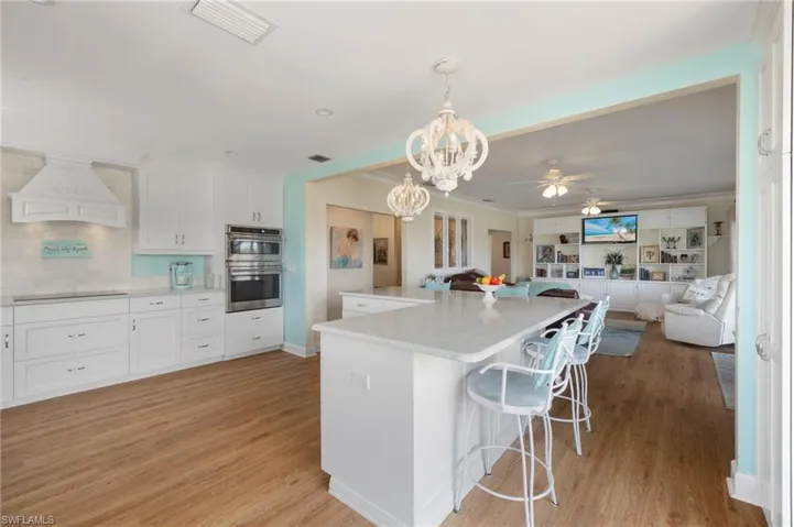 Kitchen featuring ceiling fan, white cabinets, decorative light fixtures, light wood-style flooring, and crown molding