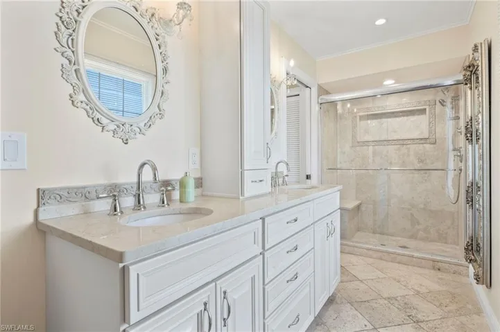 Bathroom featuring a stall shower, double vanity, and stone tile flooring