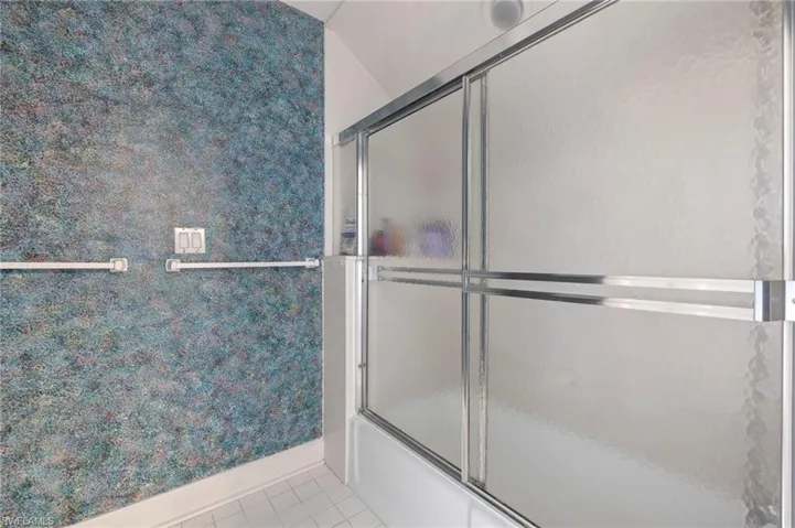 Bathroom with light tile patterned floors, wallpapered walls, and shower / bath combination with glass door