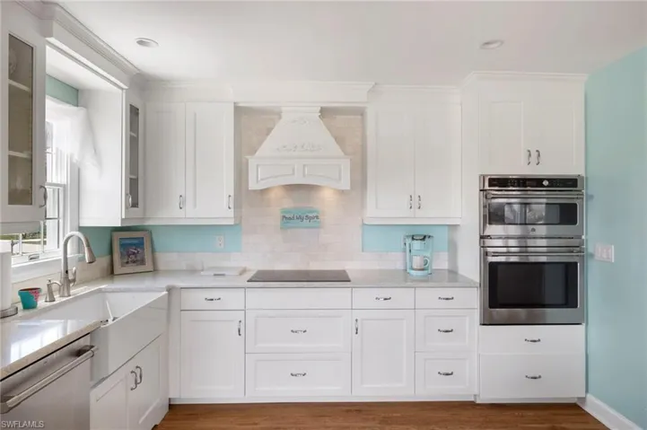 Kitchen featuring white cabinets, premium range hood, stainless steel appliances, light stone countertops, and dark wood-type flooring