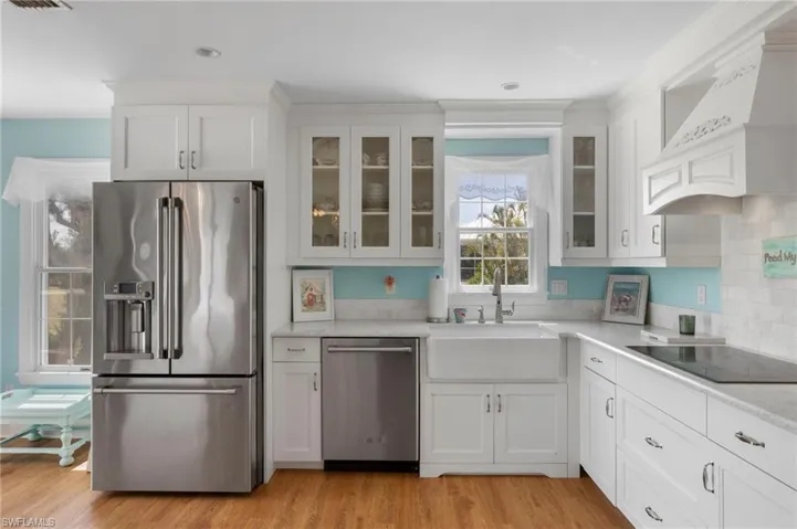 Kitchen featuring appliances with stainless steel finishes, white cabinets, light wood-type flooring, and custom range hood