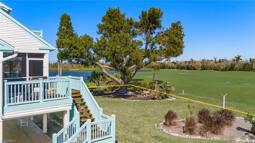 View of green lawn featuring stairs, a deck with water view, golf course view, and a sunroom