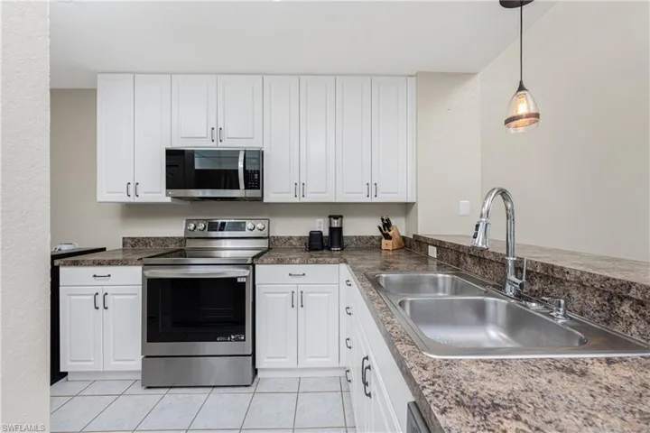 Kitchen with pendant lighting, white cabinetry, sink, light tile patterned floors, and stainless steel appliances