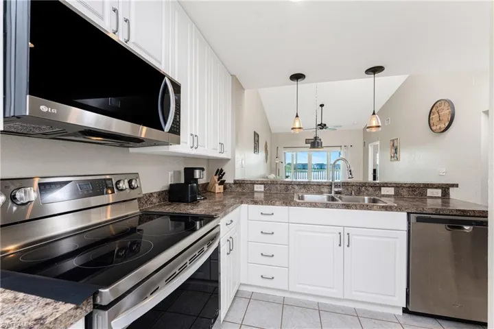 Kitchen featuring stainless steel appliances, white cabinetry, sink, and decorative light fixtures