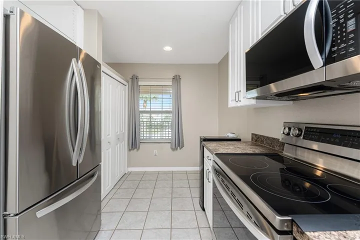 Kitchen featuring appliances with stainless steel finishes, light tile patterned floors, and white cabinets