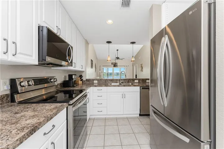 Kitchen with sink, light tile patterned floors, appliances with stainless steel finishes, white cabinets, and decorative light fixtures