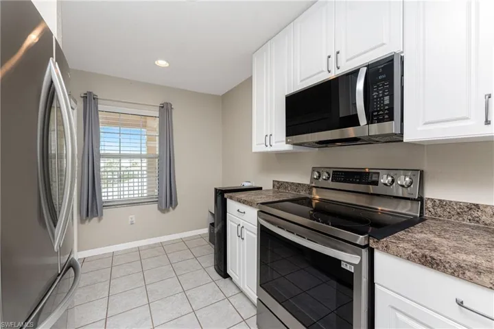 Kitchen with appliances with stainless steel finishes, light tile patterned floors, and white cabinets