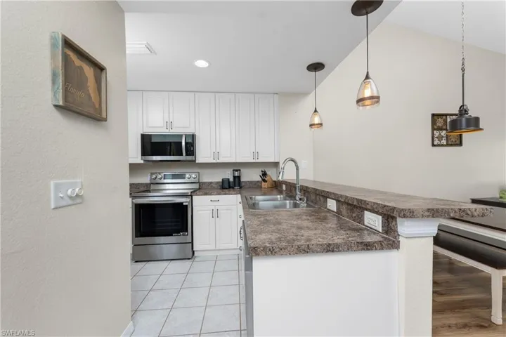 Kitchen with sink, appliances with stainless steel finishes, hanging light fixtures, white cabinets, and kitchen peninsula