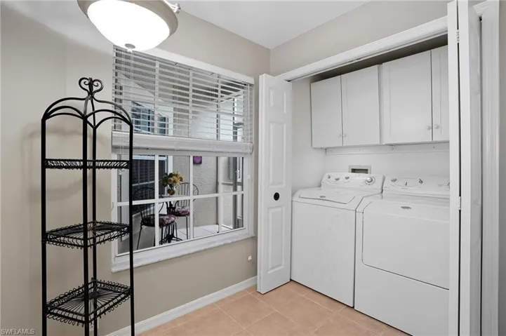 Dedicated utility area featuring tile flooring, a large window with blinds, and a built-in laundry closet with bifold doors