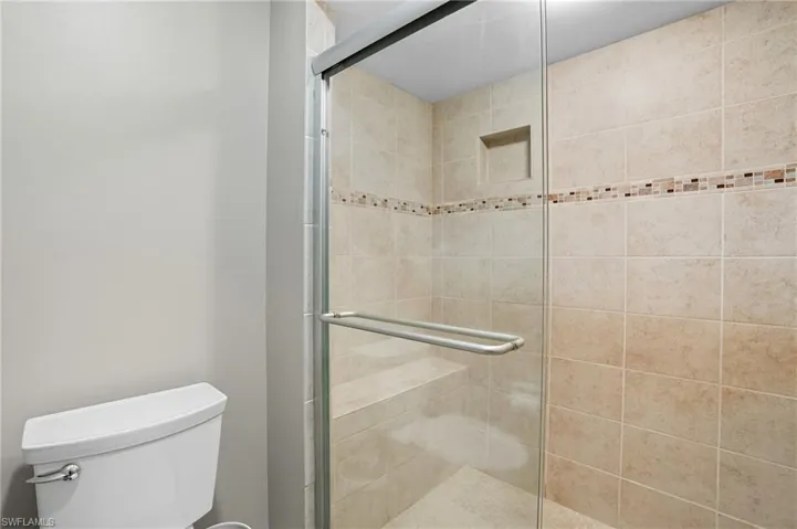 Glass-enclosed shower with a tiled interior, a built-in bench, a recessed niche, and a decorative mosaic tile band