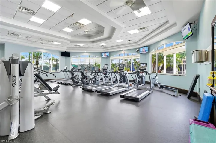 Fitness center featuring large arched windows, recessed lighting, ceiling fans, light blue wall paint, and dark gray resilient flooring