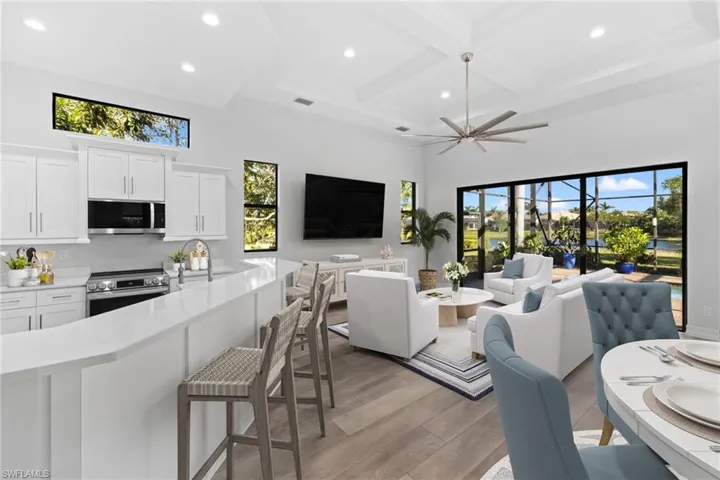 Living room featuring light wood-type flooring, coffered ceiling, ceiling fan, beamed ceiling, and a high ceiling