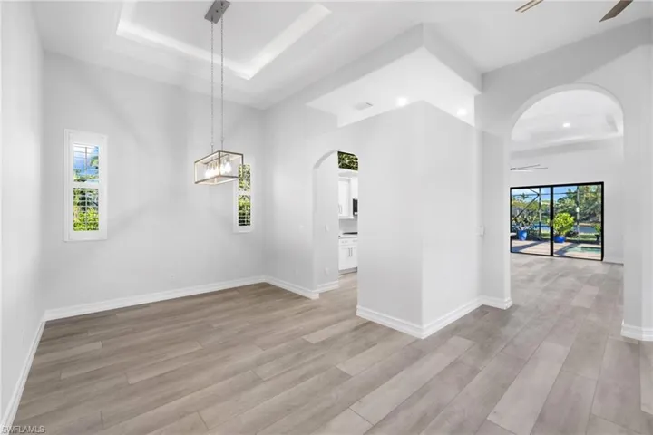 Spare room with ceiling fan with notable chandelier, a raised ceiling, and light hardwood / wood-style flooring