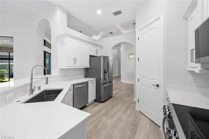 Kitchen with white cabinetry, sink, ceiling fan, stainless steel appliances, and light hardwood / wood-style flooring