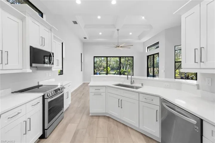 Kitchen featuring white cabinets, stainless steel appliances, sink, light hardwood / wood-style flooring, and beamed ceiling