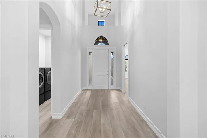 Corridor featuring separate washer and dryer, light hardwood / wood-style floors, a high ceiling, and a notable chandelier