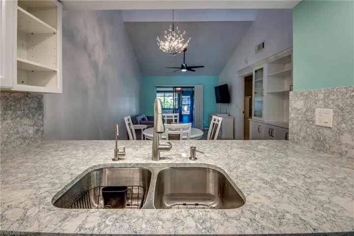 Kitchen featuring a chandelier, a sink, vaulted ceiling, decorative backsplash, and light stone countertops