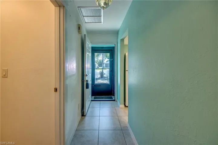 Hallway featuring light tile patterned flooring, baseboards, and a textured wall