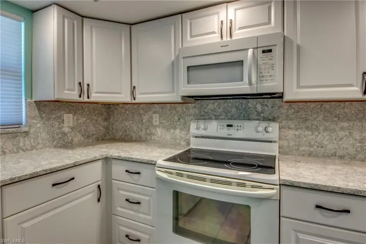 Kitchen with white appliances, white cabinetry, light countertops, and tasteful backsplash