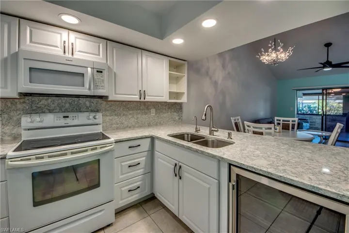 Kitchen featuring white appliances, a sink, beverage cooler, recessed lighting, and white cabinets