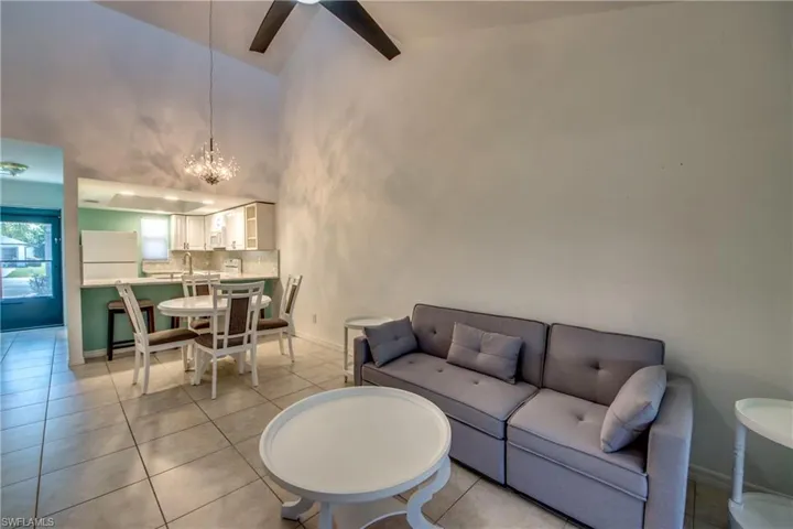 Living area with a chandelier, high vaulted ceiling, ceiling fan, light tile patterned floors, and baseboards