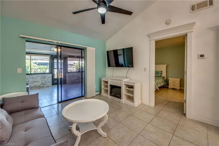 Living area with a ceiling fan, vaulted ceiling, light tile patterned floors, baseboards, and a glass covered fireplace