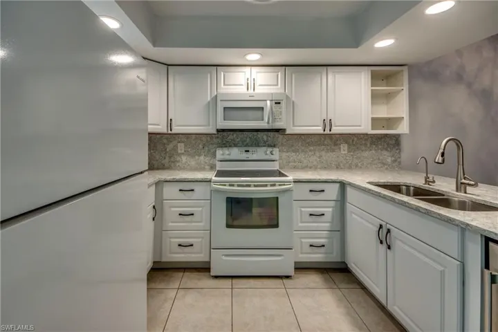 Kitchen featuring white appliances, a sink, light tile patterned flooring, backsplash, and white cabinets