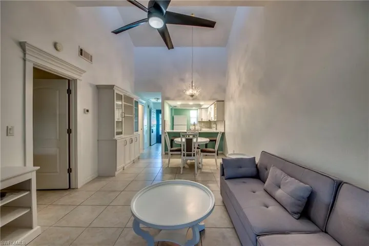 Living area with high vaulted ceiling, light tile patterned floors, a chandelier, and a ceiling fan