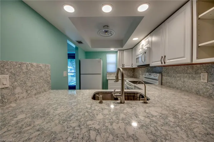 Kitchen featuring white appliances, a sink, light stone countertops, backsplash, and white cabinetry