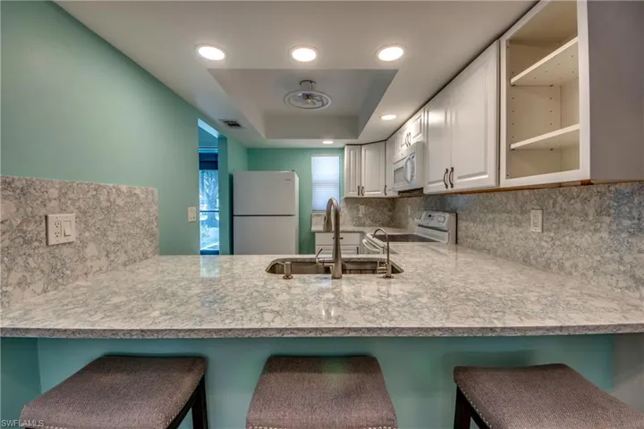 Kitchen featuring white appliances, a sink, decorative backsplash, a raised ceiling, and a peninsula