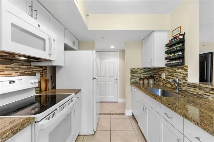Kitchen with white appliances, dark stone countertops, white cabinetry, and sink