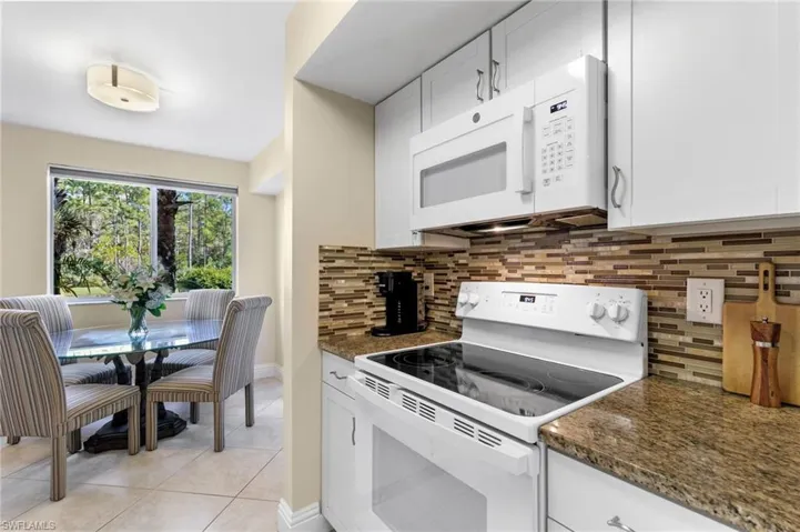 Kitchen featuring white appliances, decorative backsplash, dark stone countertops, white cabinets, and light tile patterned flooring