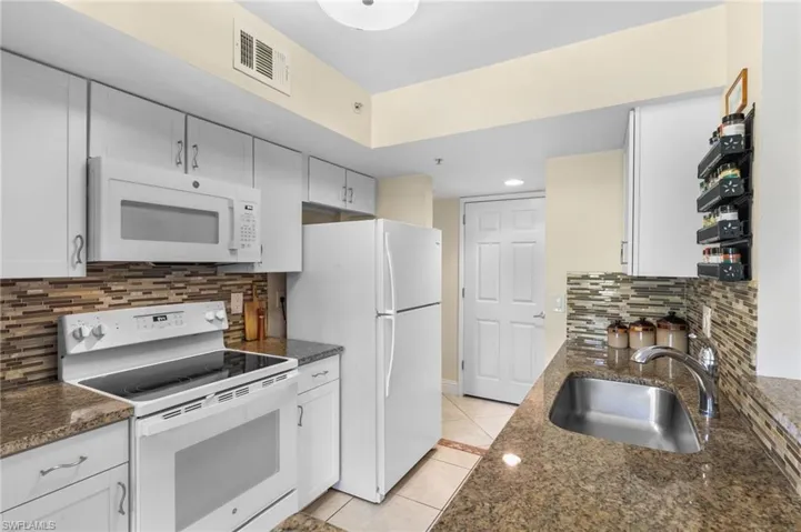 Kitchen featuring white cabinets, light tile patterned floors, white appliances, sink, and tasteful backsplash