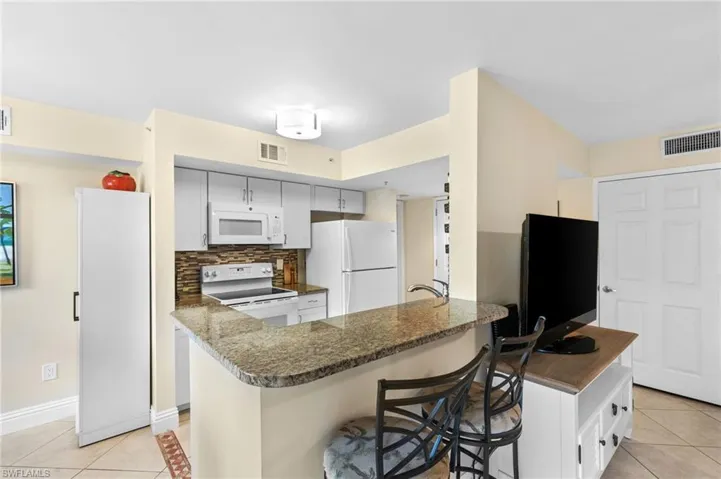 Kitchen featuring a breakfast bar, kitchen peninsula, white appliances, and light tile patterned flooring