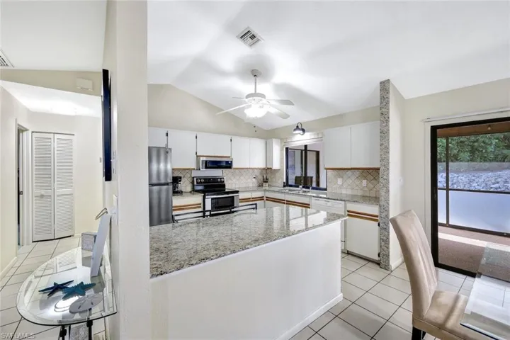 Kitchen with light tile patterned flooring, ceiling fan, decorative backsplash, appliances with stainless steel finishes, and lofted ceiling