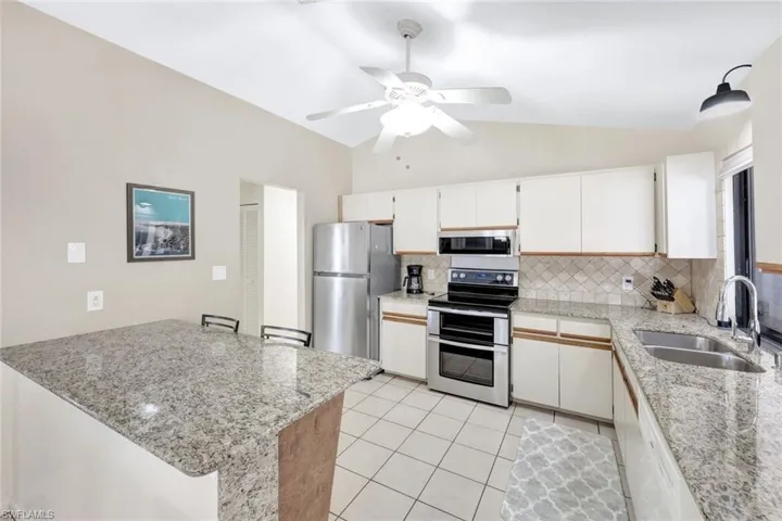 Kitchen with light tile patterned flooring, lofted ceiling, tasteful backsplash, stainless steel appliances, and sink